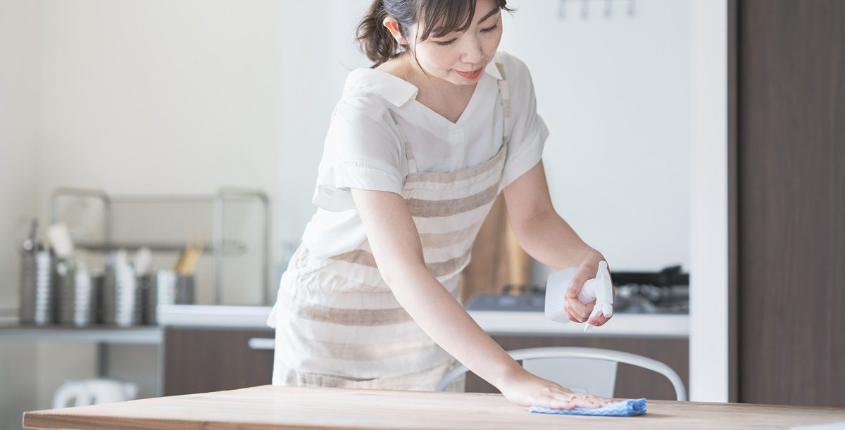 Asian woman disinfecting home dining table with spray
