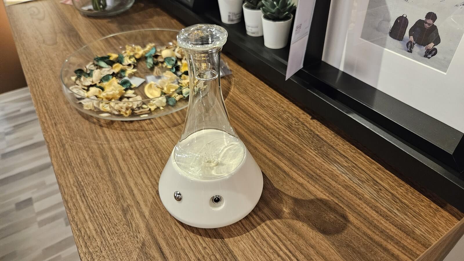 白色錐瓶造型的不用加水擴香儀,旁邊放著一碗乾燥香氛花材
